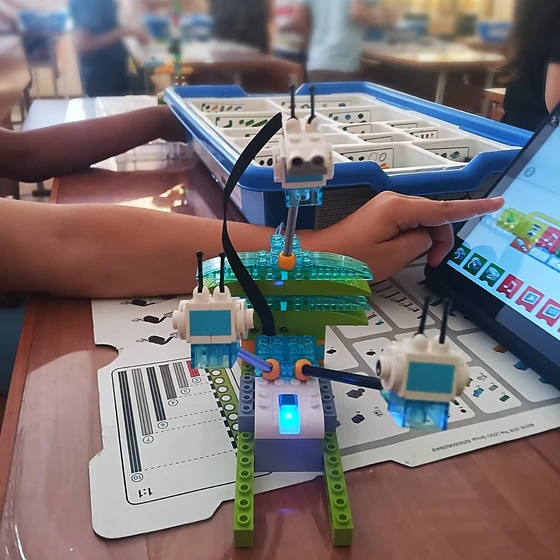 Готов робот от LEGO Education със светещо блокче, дете сочи програмата на таблета