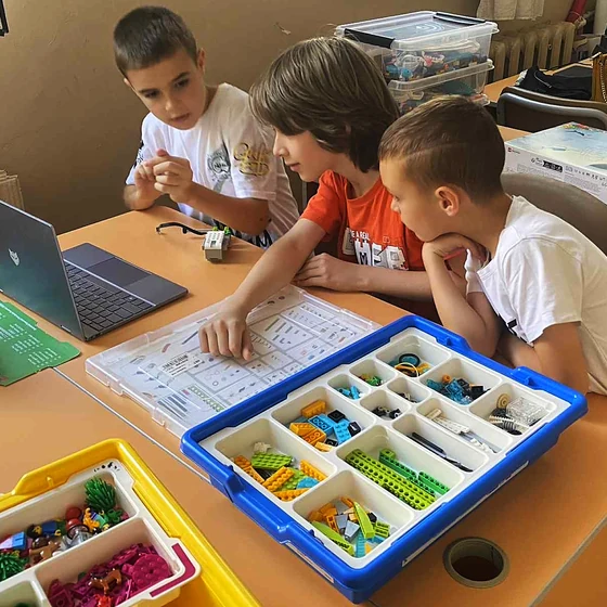 Три момчета следят екрана на лаптопа, докато сглобяват модел от LEGO Education