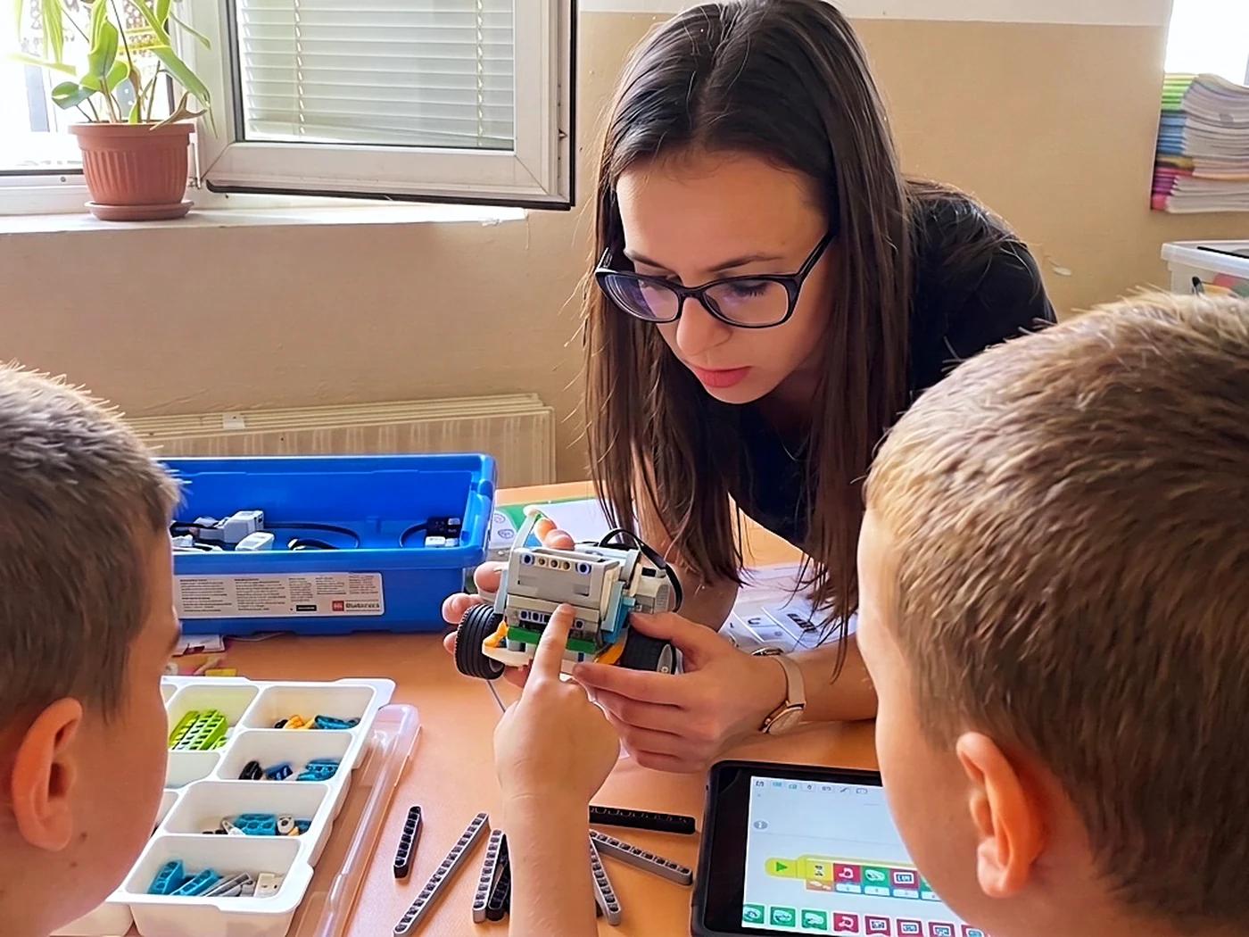 Даниела помага на две деца да сглобят робот от LEGO Education